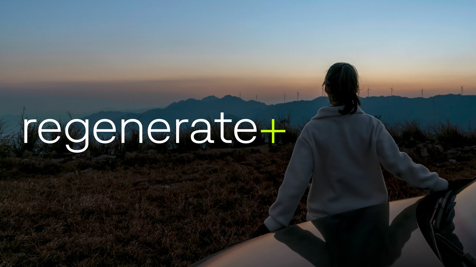 Person leaning on a car watching a sunset over a mountain landscape with wind turbines; the image is titled 'regenerate+'.