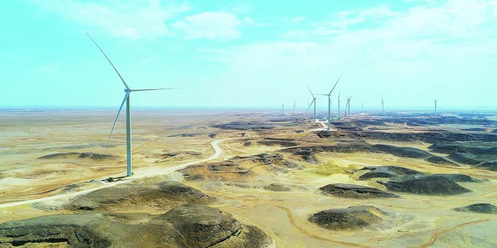 Landscape view of multiple wind turbines in a dry, hilly desert area.